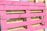 A wooden pallet painted in bright pink, with natural wood color visible in the background. The pallet is leaning against other unpainted pallets, showing a contrast between the vivid pink and the neutral tones of wood.