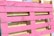 A wooden pallet painted in bright pink, with natural wood color visible in the background. The pallet is leaning against other unpainted pallets, showing a contrast between the vivid pink and the neutral tones of wood.