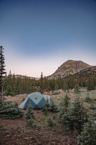 A rugged camper setting up a tent at sunset with mountains in the background.