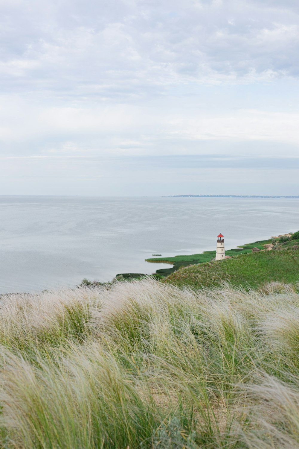 um farol em uma colina gramada com vista para o oceano
