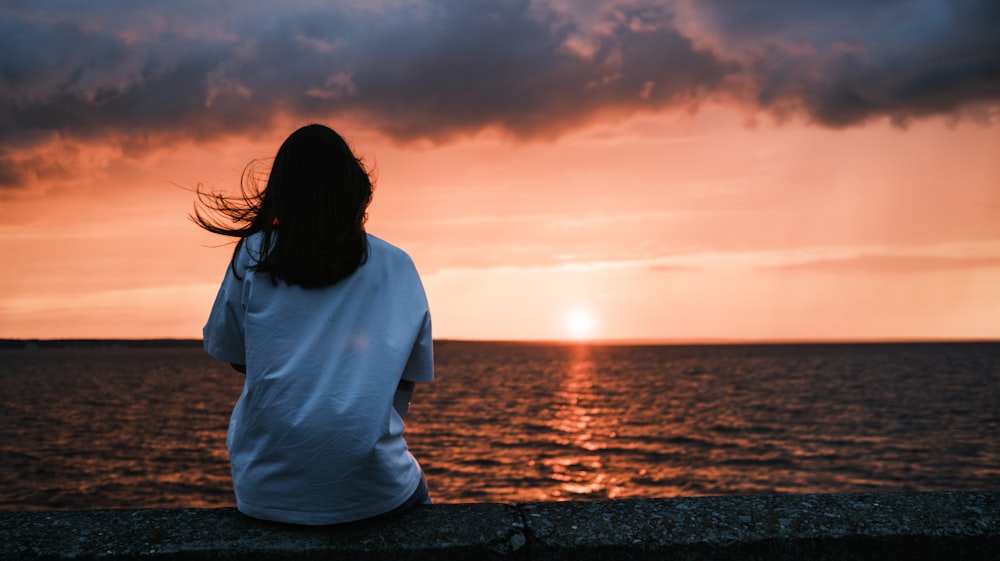 a woman sitting on a wall looking out at the ocean