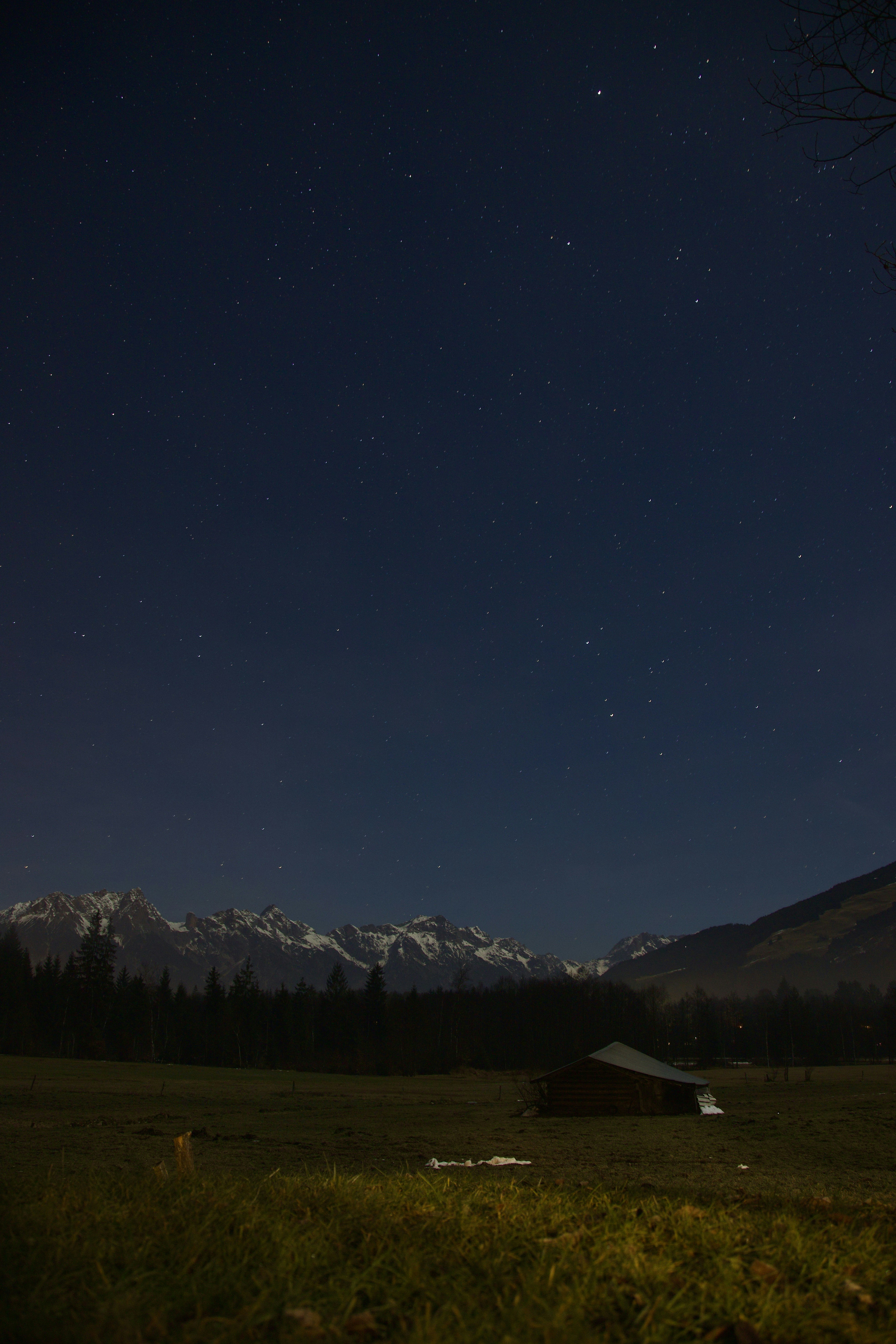 A small wooden hut sits in a field under a starry night sky.