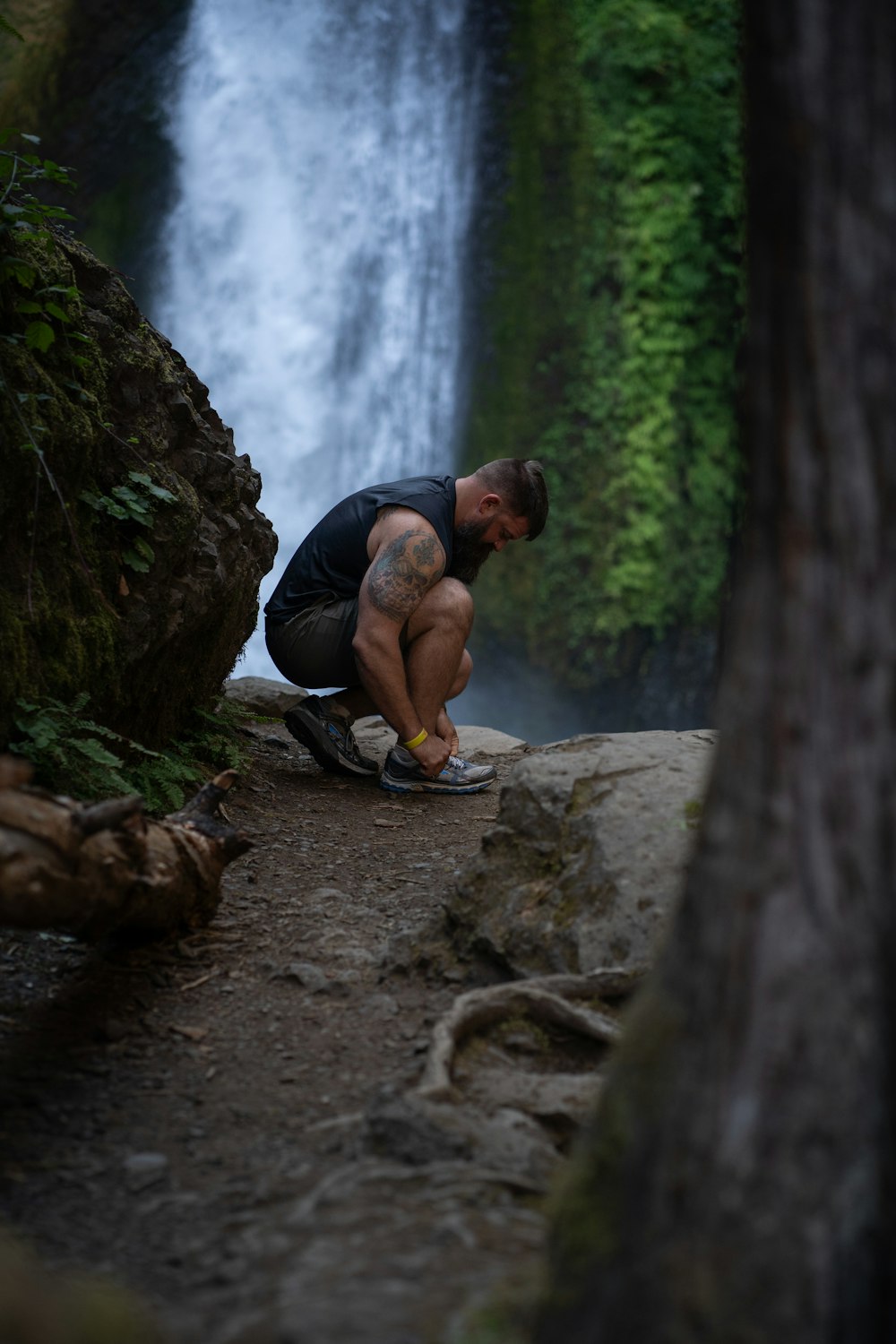 a man squatting on a rock in front of a waterfall