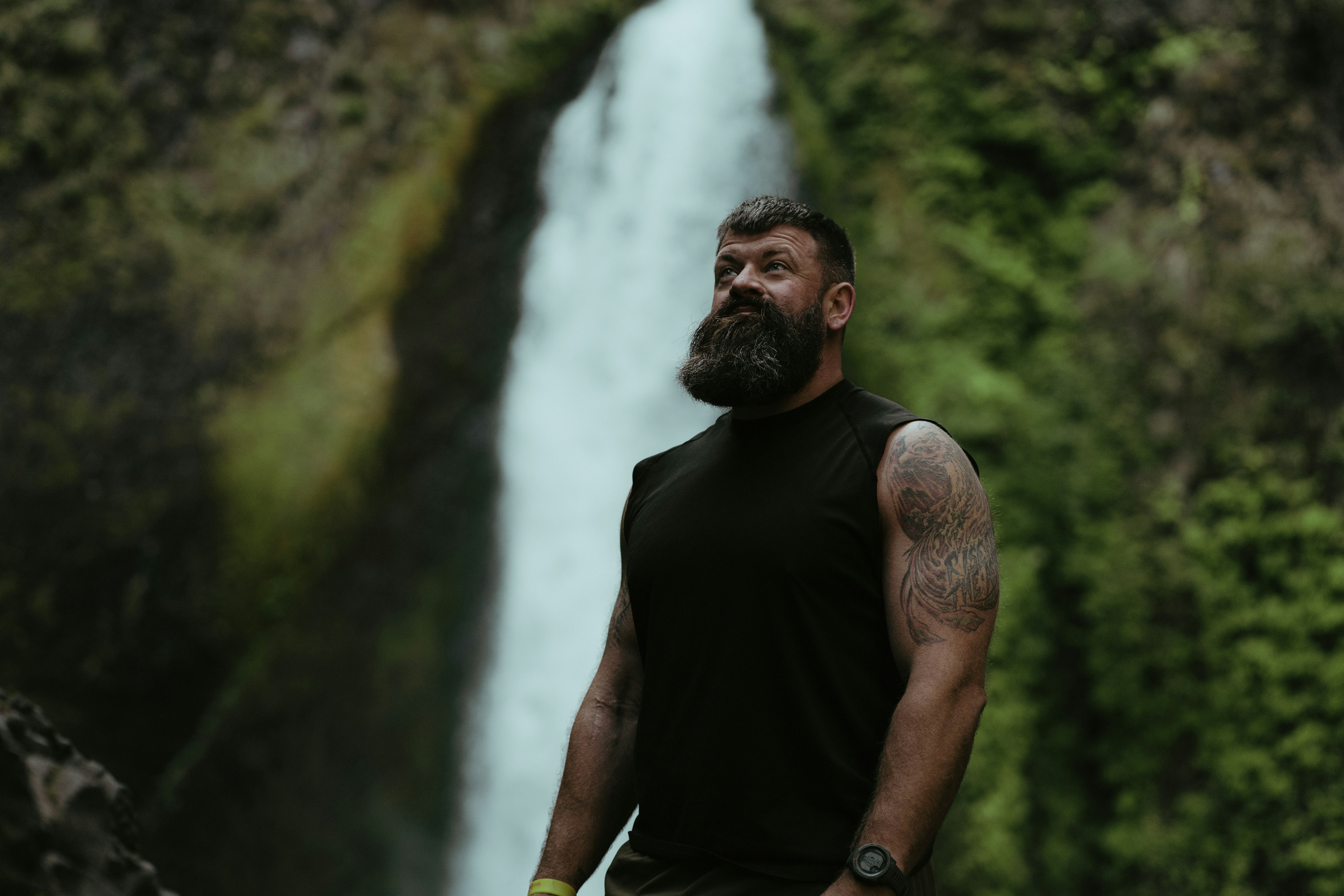 a man with a beard standing in front of a waterfall