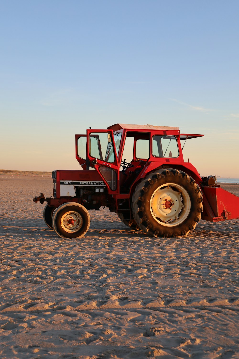 a red tractor parked on top of a sandy beach