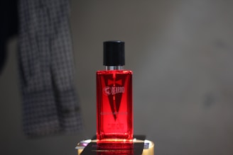 A sleek black and red perfume bottle labeled 'Stud' for men, set against a gray background.
