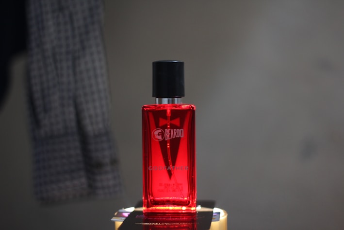 A sleek black and red perfume bottle labeled 'Stud' for men, set against a gray background.
