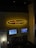 A bar and grill setting features a prominently lit sign reading 'Red Embers Bar & Grill' with a flame design. Below the sign, two mounted televisions display different sports events. The setting includes dim lighting with a modern interior, featuring stone accents and seating areas.