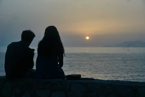 Couple sharing a quiet moment on deck, the sun dipping just behind the water’s edge, bathing everything in soft sand tones.
