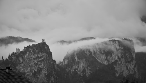 A dramatic black-and-white photo of a misty castle perched atop a rugged cliff.