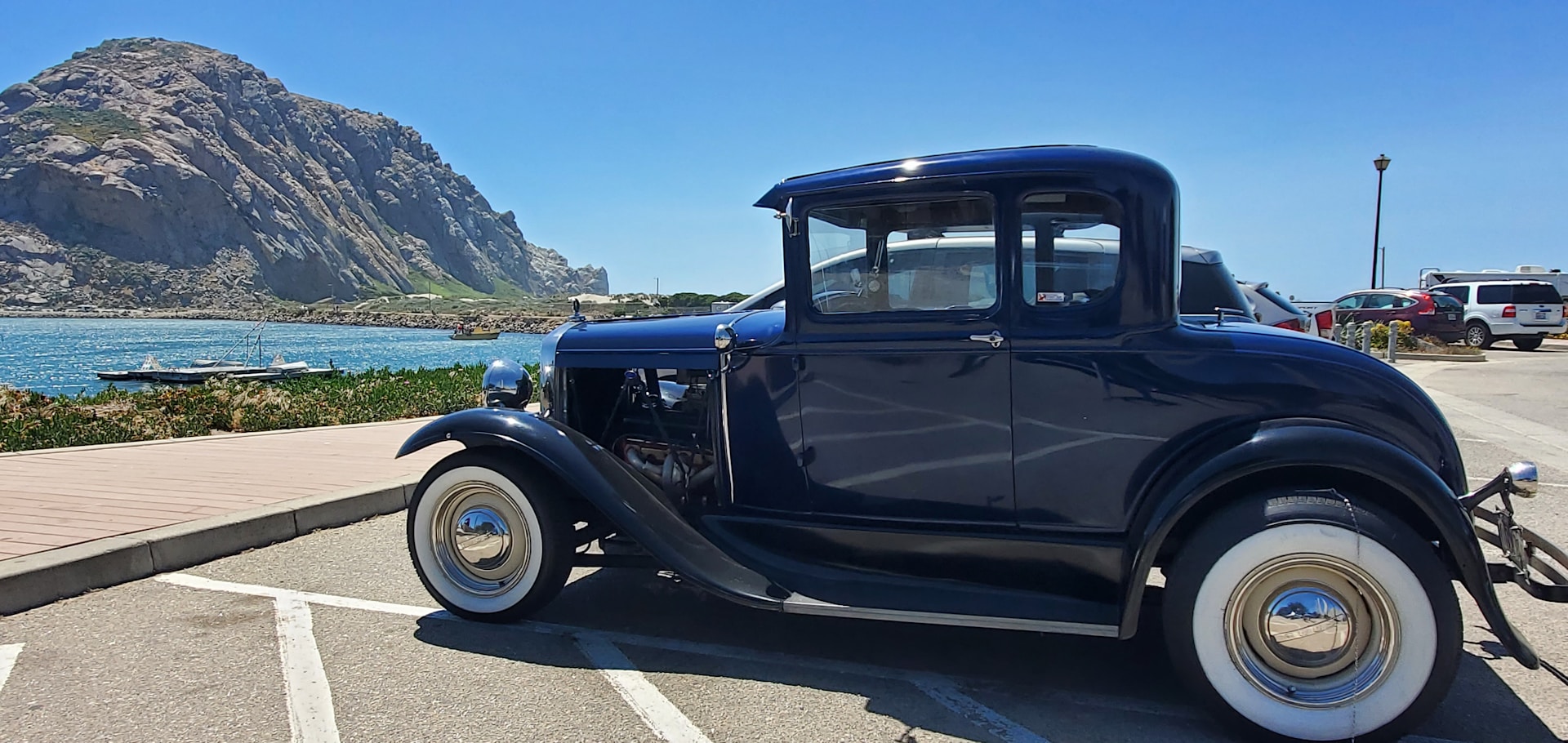 A classic 1955 Chrysler road race car parked on a scenic coastal road, showcasing its sleek lines and vintage design.