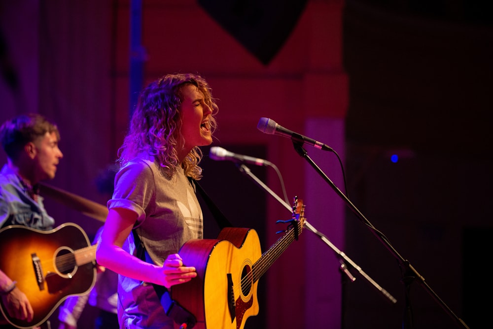 a woman singing into a microphone while holding a guitar