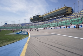 Wide shot of a packed MotoGP grandstand with cheering fans under a bright sky.
