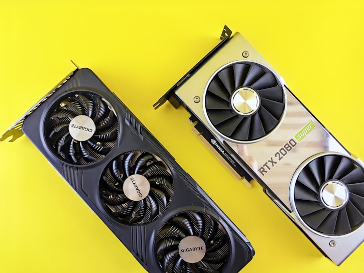 Two graphics cards are placed against a bright yellow background. The card on the left is a Gigabyte model with three fans, featuring a sleek, black design. The card on the right is an RTX 2080 Super, with a metallic finish and dual fans.