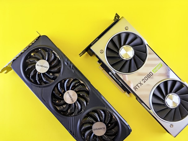 Two graphics cards are placed against a bright yellow background. The card on the left is a Gigabyte model with three fans, featuring a sleek, black design. The card on the right is an RTX 2080 Super, with a metallic finish and dual fans.