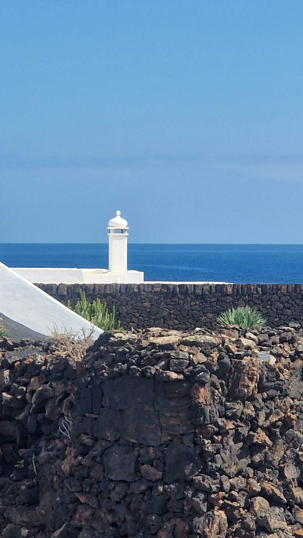 a white umbrella sitting on top of a stone wall next to the ocean