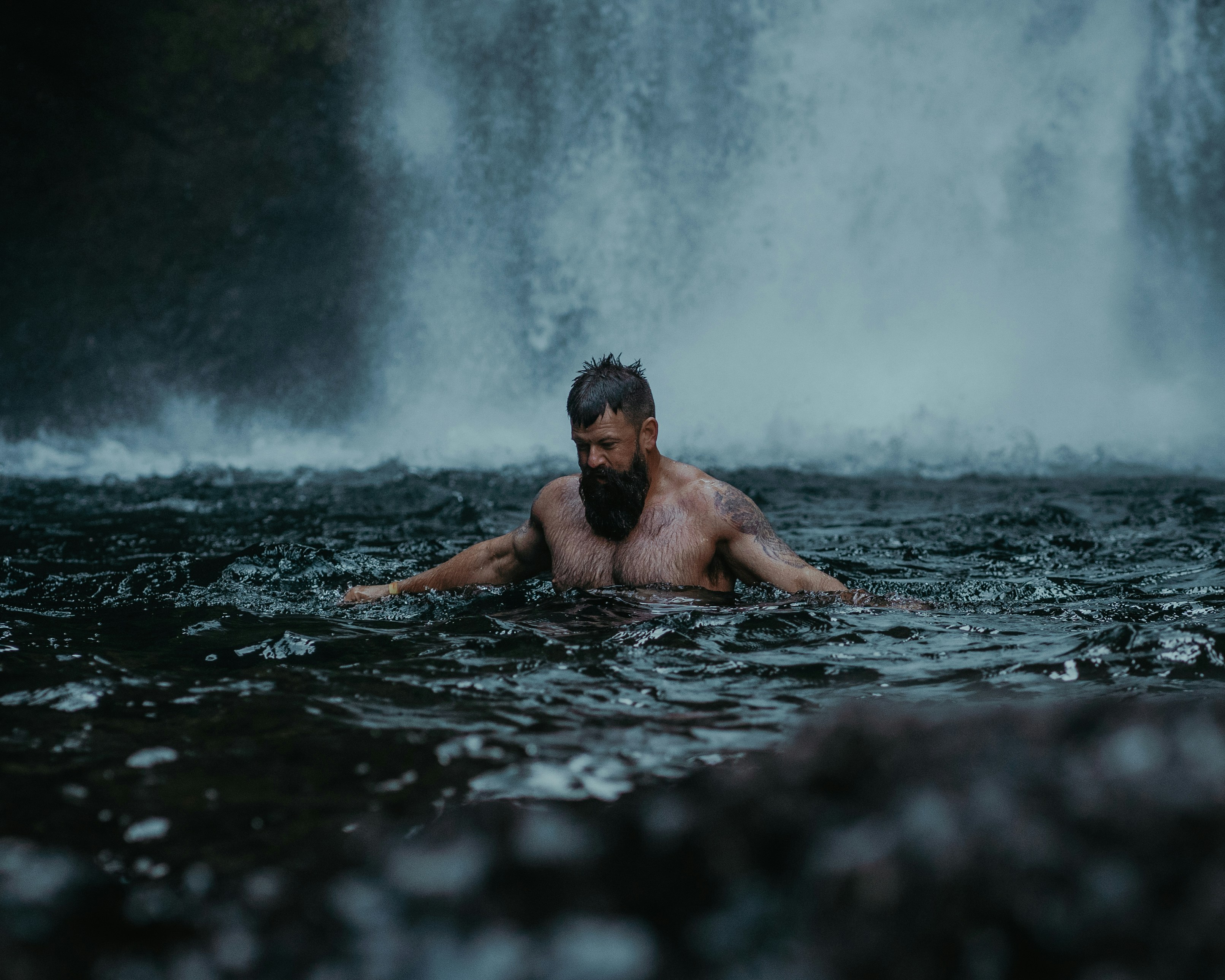 Candid photo of a tattooed bearded man in water next to a waterfall. Photo by Lance Reis / KickassDesigns on IG