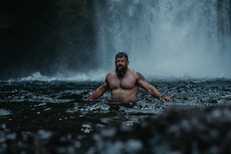 a man standing in the water in front of a waterfall