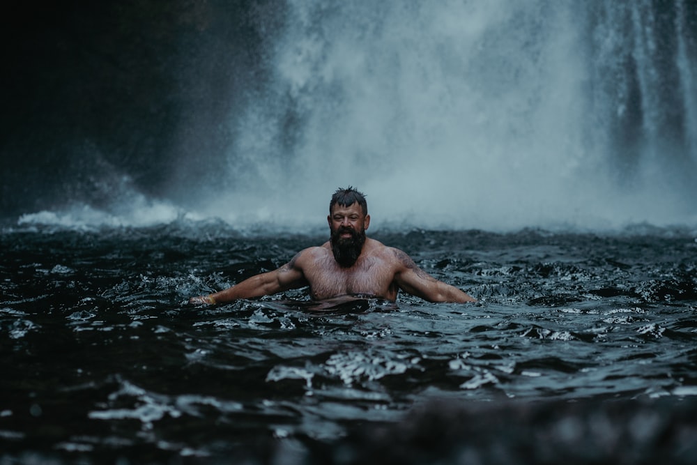 a man in a body of water in front of a waterfall