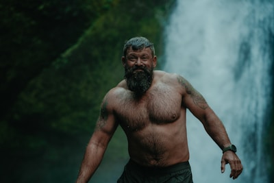 a man with a beard standing in front of a waterfall