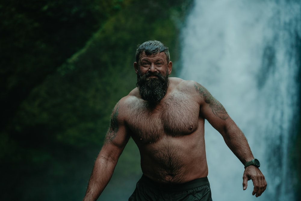 a man with a beard standing in front of a waterfall