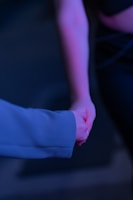 Couple holding hands, bathed in blush pink and deep maroon light.