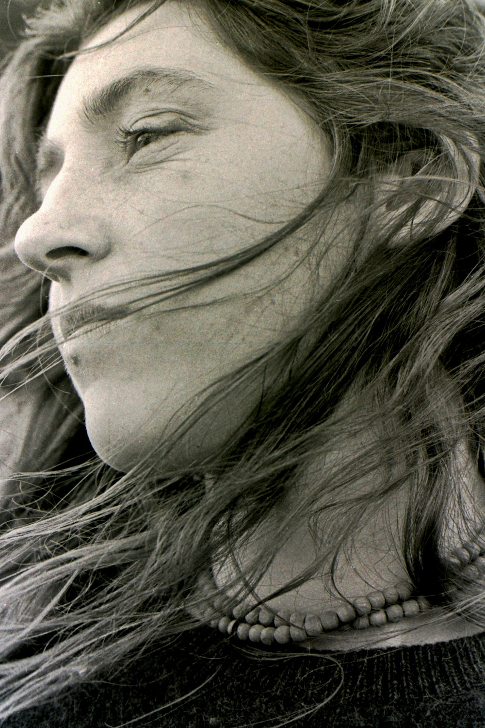 a black and white photo of a woman with her hair blowing in the wind