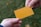 Two hands are exchanging a plain orange rectangular card against a blurred green background. The card is centrally positioned, held by fingers from each hand.