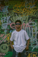 Side profile of a person walking past graffiti walls, showcasing a premium white t-shirt with subtle branding.