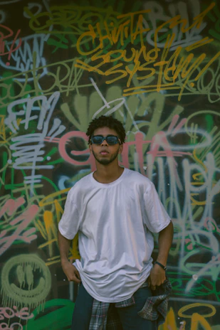 A model wearing a relaxed-fit shirt with cheeky text and colorful splashes, standing on a graffiti-covered New York street corner.