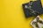 Two gift boxes with ribbons are placed on a bright yellow background. The upper box is black with a black ribbon, while the lower box is silver with a brown ribbon.