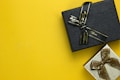 Two gift boxes with ribbons are placed on a bright yellow background. The upper box is black with a black ribbon, while the lower box is silver with a brown ribbon.