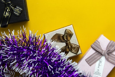 a gift wrapped in gold and silver ribbon next to a purple tinsel