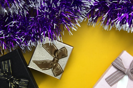 Several gift boxes with ribbon bows, placed on a bright yellow background, surrounded by purple and white tinsel.