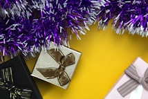 Several gift boxes with ribbon bows, placed on a bright yellow background, surrounded by purple and white tinsel.