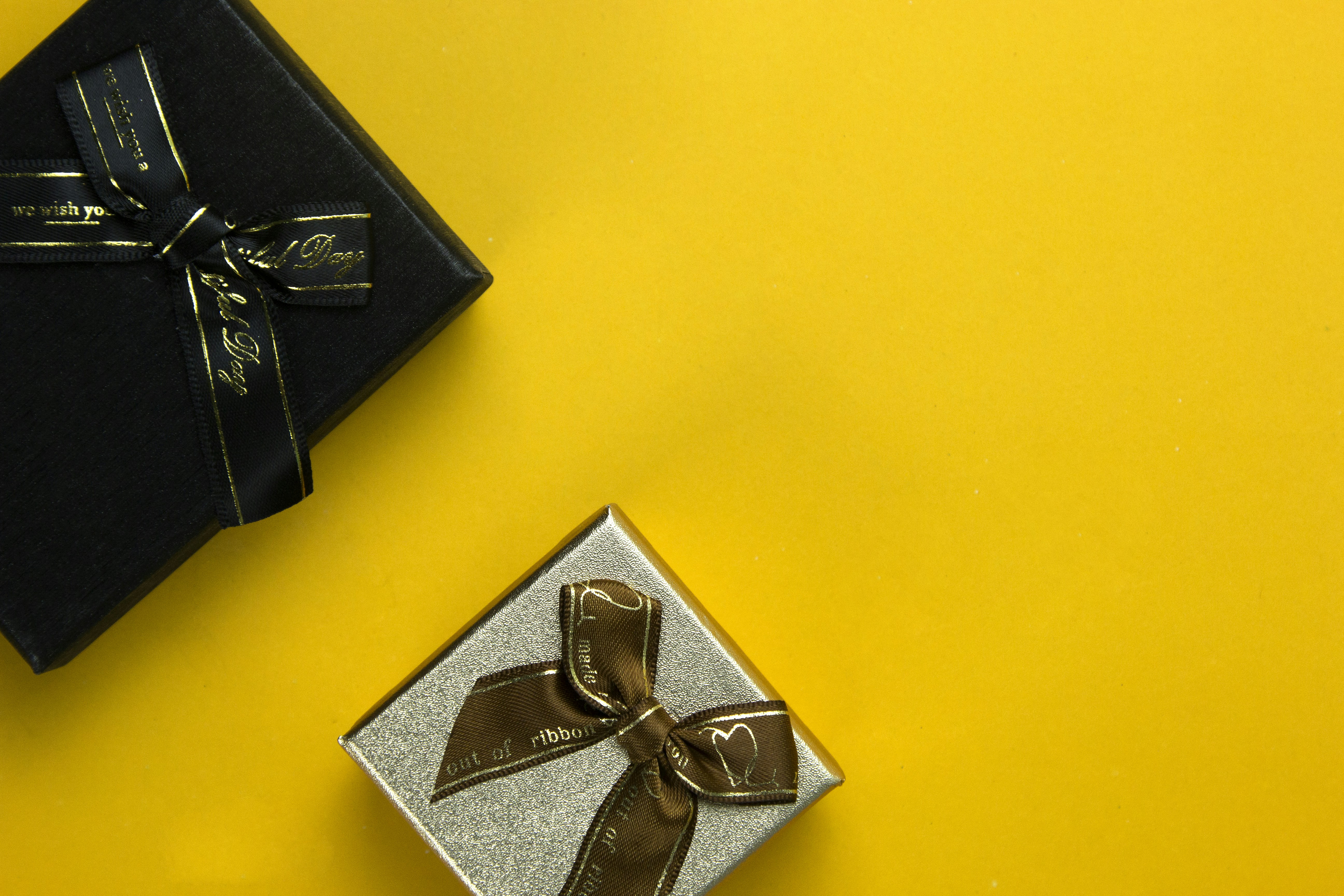 a black box with a gold ribbon and a silver box with a brown bow