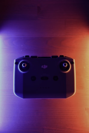 A close-up of a high-tech drone controller illuminated by cyan blue light in a dark studio.