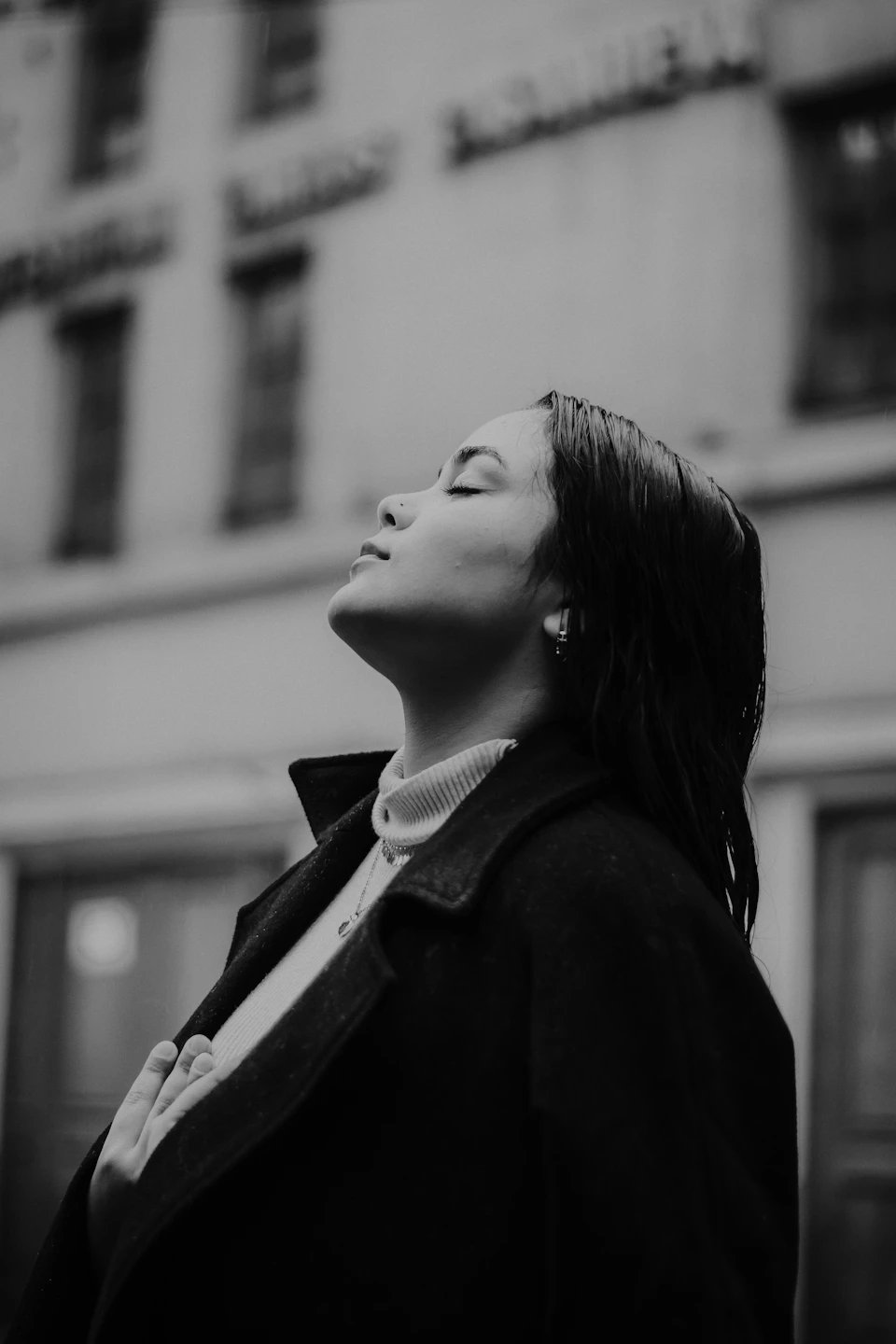 Woman standing on street with head tilted back and eyes closed in contemplation