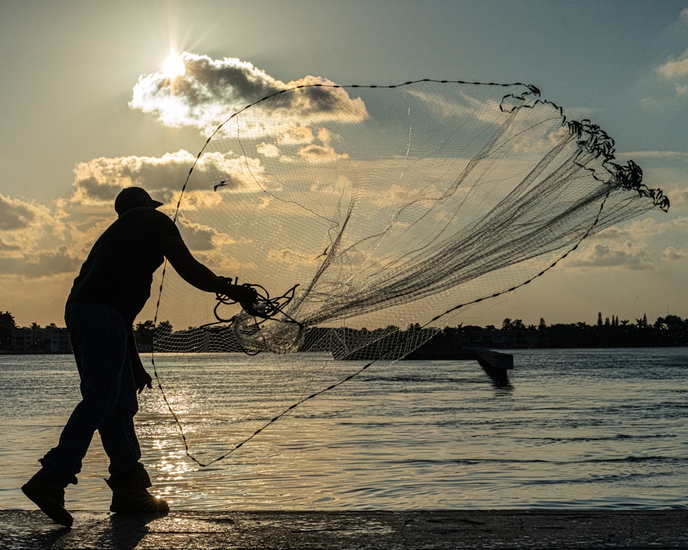 Un hombre parado en una playa sosteniendo una red de pesca