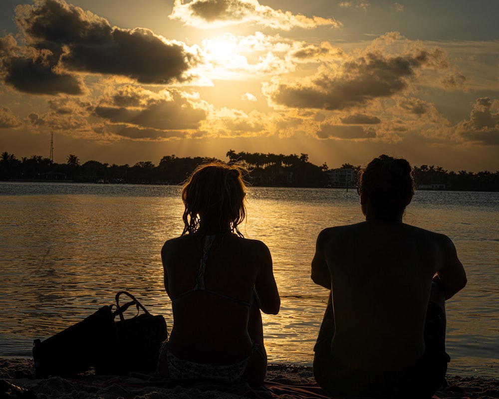 two people sitting on a beach watching the sun set