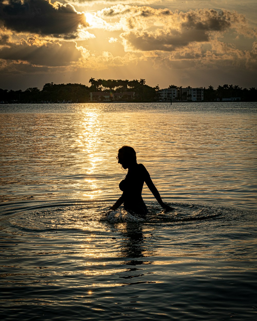 a woman wading in the water at sunset