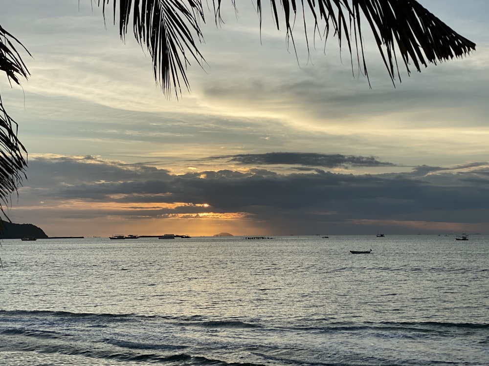 the sun is setting over the ocean with boats in the water