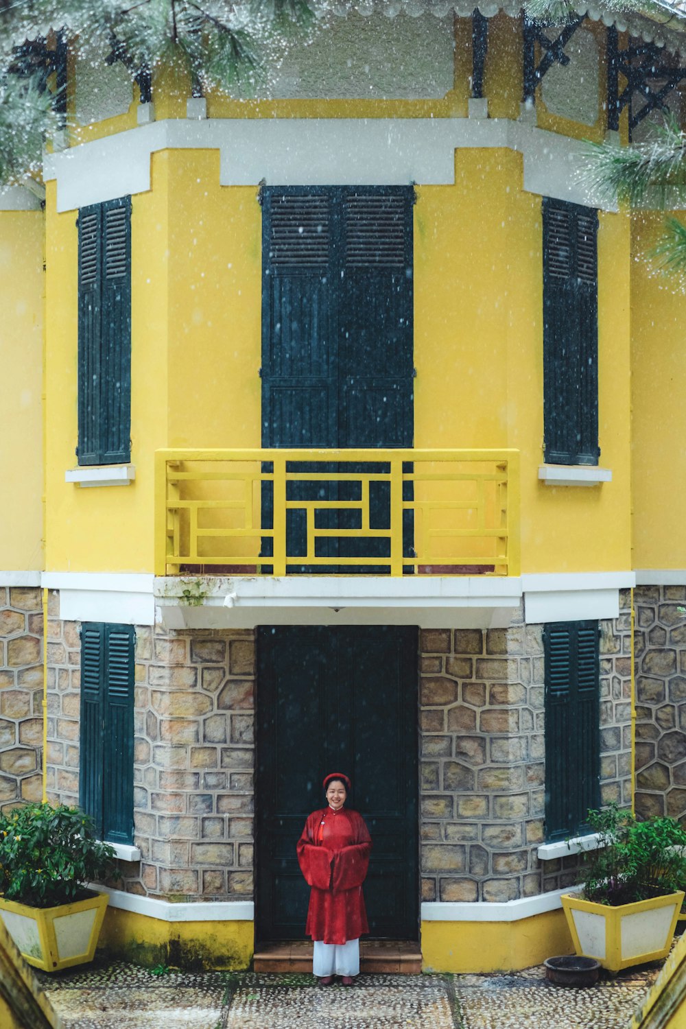 a person in a red coat standing in front of a yellow building