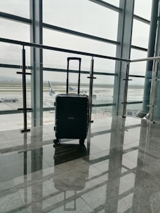 A sleek suitcase standing beside a busy airport terminal entrance.