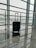 A suitcase stands on a shiny marble floor near large glass windows at an airport terminal. An airplane is visible outside on the tarmac.