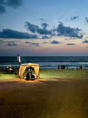 A cozy beachside cabana with tourists relaxing by the turquoise sea at sunset.
