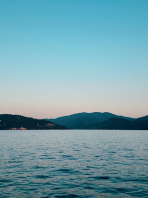 Watercolor scene of a calm lake reflecting a pale blue sky with subtle ripples.