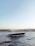 A sleek, modern yacht is gliding through a body of water with gentle waves. In the background, a cityscape featuring historic architecture, including minarets and domes, can be seen under a clear blue sky, creating a serene and picturesque scene.