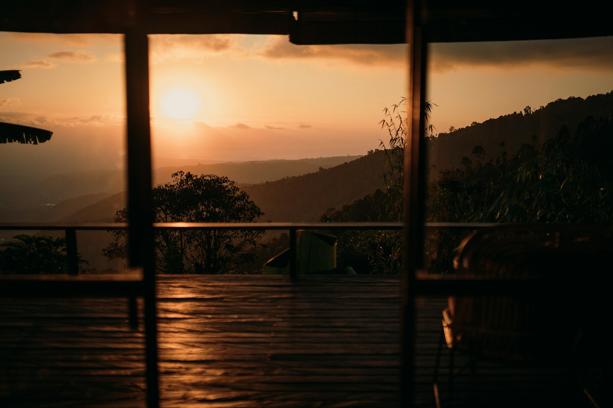 Sunset over forested hills seen from inside a luxury lodge, through a doorway onto a wooden deck