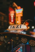 A taxi sign is prominently displayed, surrounded by a blur of colorful neon lights in the background, giving an urban nighttime vibe.